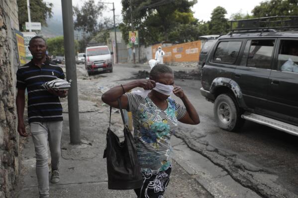 A woman walks past local authorities removing the bodies of men that were set on fire by a mob in Port-au-Prince, Haiti, Tuesday, April 25, 2023, a day after a mob pulled the 13 suspected gang members from police custody at a traffic stop and beat and burned them to death with gasoline-soaked tires. (AP Photo/Odelyn Joseph)