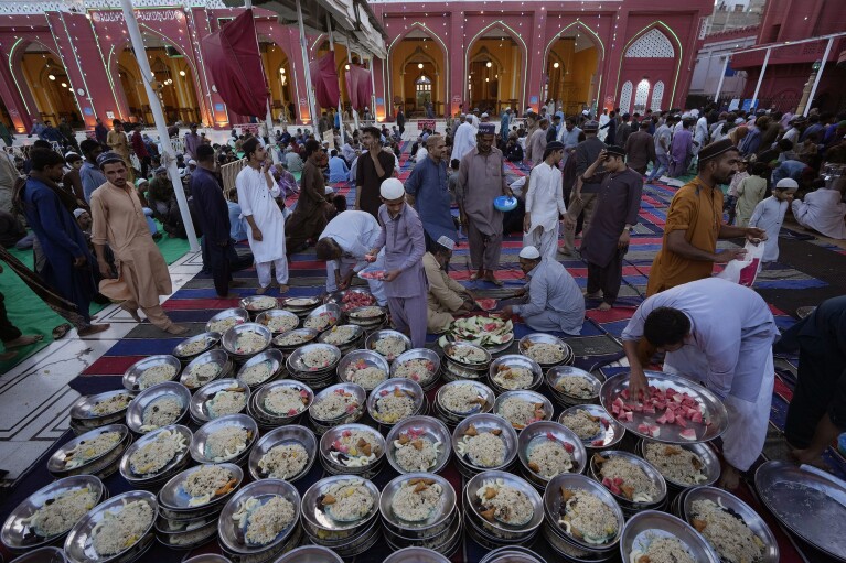 Volunteers distribute food plates among people for breaking their fast during the Muslim's holy fasting month of Ramadan, at Memon mosque in Karachi, Pakistan, Tuesday, March 12, 2024. (AP Photo/Fareed Khan)