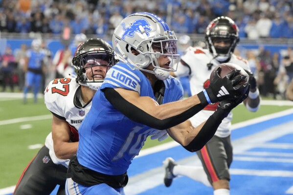 Detroit Lions wide receiver Amon-Ra St. Brown, foreground, catches a touchdown pass in front of Tampa Bay Buccaneers cornerback Zyon McCollum (27) during the second half of an NFL football NFC divisional playoff game, Sunday, Jan. 21, 2024, in Detroit. (AP Photo/Carlos Osorio)