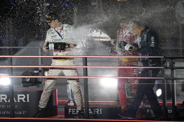 CORRECTS THAT THE PHOTO SHOWS VERSTAPPEN AT LEFT, SERGIO PEREZ AT CENTER AND PERSON AT RIGHT IS UNIDENTIFIED - Red Bull driver Max Verstappen, of the Netherlands, left, Sergio Perez, of Mexico, center, and an unidentified person at right, celebrate after a first and second place finish during the Formula One Las Vegas Grand Prix auto race, Sunday, Nov. 19, 2023, in Las Vegas. (AP Photo/John Locher)