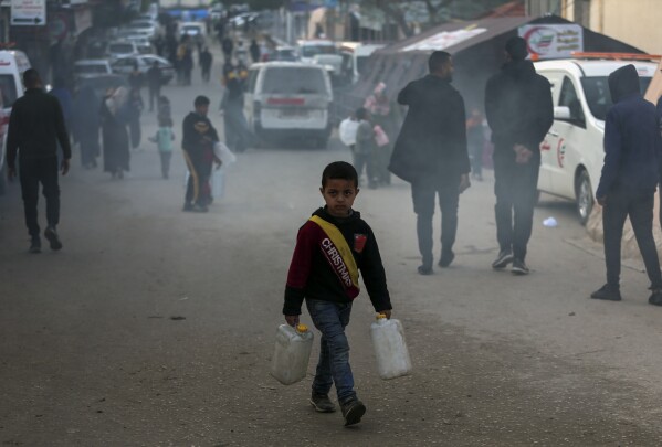 A Palestinian child displaced by the Israeli ground offensive on the Gaza Strip carries jerry cans at a makeshift tent camp in Rafah, Gaza Strip, Monday, Feb. 19, 2024. (AP Photo/Mohammed Dahman)