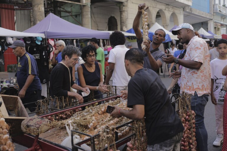Shoppers gather round a cart of garlic at a street market in Havana, Cuba, Saturday, March 16, 2024. Without a functioning market economy, Cuban agriculture has long measured itself by socialist production goals that it has rarely been able to meet. (AP Photo/Ariel Ley)