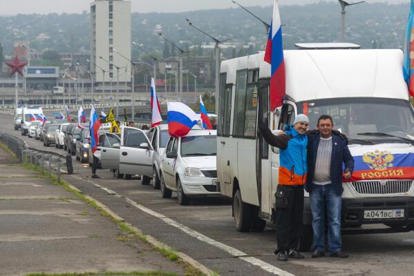 Two men pose for a photo in front of motorcade organized to support voting in a referendum in Luhansk, eastern Ukraine, Friday, Sept. 23, 2022. Voting began Friday in four Moscow-held regions of Ukraine on referendums to become part of Russia. (AP Photo)