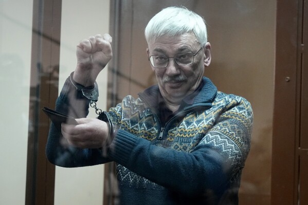 FILE – Oleg Orlov, the co-chair of the Memorial Human Rights Center, gestures inside a defendants’ cage in a court in Moscow, Russia, on Tuesday, Feb. 27, 2024. Over the last decade, Vladimir Putin's Russia evolved from a country that tolerates at least some dissent to one that ruthlessly suppresses it. Arrests, trials and long prison terms — once rare — are commonplace. (AP Photo, File)