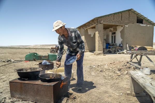 A man cooks fish caught from the remnants of the Aral Sea in a desert outside Muynak, Uzbekistan, Saturday, June 24, 2023. (AP Photo/Ebrahim Noroozi)