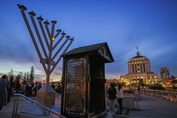 People look at a replacement menorah in Oakland, Calif., on Wednesday, Dec. 13, 2023, at the Lake Merritt Amphitheater after the first one was vandalized. Hundreds of people gathered to relight the menorah after the first one was vandalized and its pieces dismantled and strewn about, prompting the Oakland Police Department to launch a hate crime investigation earlier in the day. (Ray Chavez/Bay Area News Group via AP)/Bay Area News Group via AP)