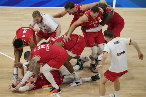 Germany guard Andreas Obst lays on the ground as teammates celebrates after winning against the United States in a Basketball World Cup semi final game in Manila, Philippines, Friday, Sept. 8, 2023. (AP Photo/Aaron Favila)
