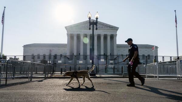 A Police officer leads a K9 around steel fencing and barricades surrounding the Supreme Court, Friday, June 24, 2022, in Washington. (AP Photo/Gemunu Amarasinghe)