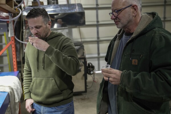 Jonathan Davis, left, tastes the first run of maple syrup with his father, Steven, right, Saturday, Feb. 24, 2024, in Sturgeon Bay, Wis. Steven Davis, who started tapping 220 trees on his family's land about six years ago, said he now feels "more like partners" with the land. (AP Photo/Joshua A. Bickel)