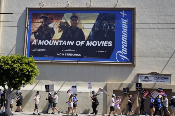 An advertisement for streaming service Paramount+ appears above striking writers and actors at rally outside Paramount studios in Los Angeles on Friday, July 14, 2023. This marks the first day actors formally joined the picket lines, more than two months after screenwriters began striking in their bid to get better pay and working conditions. (AP Photo/Chris Pizzello)