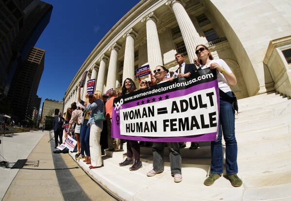 As viewed through a fisheye lens, demonstrators hold a sign on the steps before a news conference outside the United States Court of Appeals for the Tenth Circuit Tuesday, May 14, 2024, in Denver. The "Save Sisterhood" demonstration and news conference were staged after oral arguments for the landmark Westenbroek et al v. Kappa Kappa Gamma sorority lawsuit. The suit claims that the sorority violated bylaws by allowing a male to join the chapter at the University of Wyoming in 2022. (AP Photo/David Zalubowski)