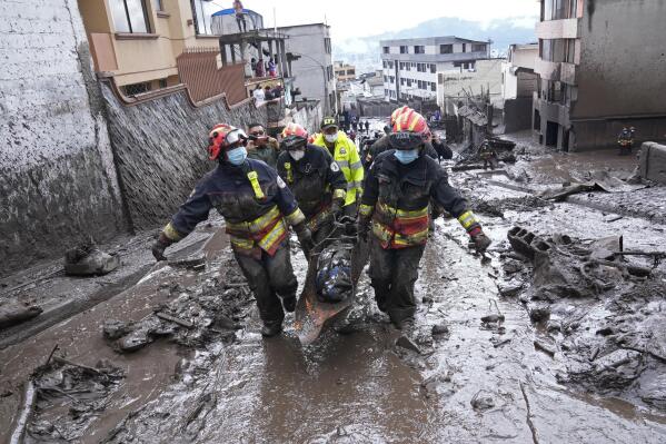 Rescue workers carry away the body of a victim after flash flooding triggered by rain filled up nearby streams that burst their containment mechanisms, collapsing a hillside and bringing waves of mud over homes in La Gasca area of Quito, Ecuador, Tuesday, Feb. 1, 2022. (AP Photo/Dolores Ochoa)