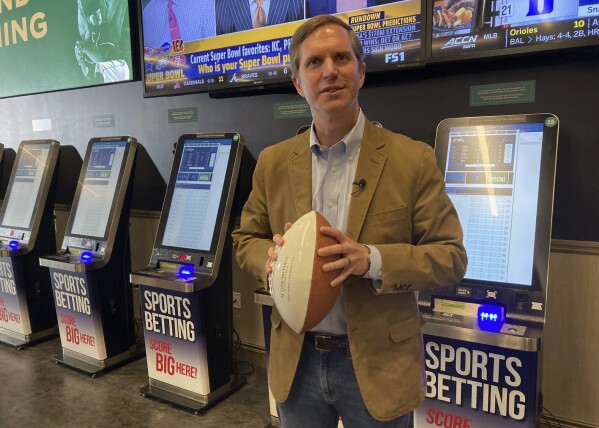 Kentucky Gov. Andy Beshear stands in front of sports betting kiosks at Churchill Downs in Louisville, Ky., Thursday, Sept. 7, 2023. The Democratic governor placed the first sports bet Thursday at Churchill Downs, home of the Kentucky Derby. It fulfilled a pledge that his administration would launch sports wagering in time for the NFL season. (AP Photo/Bruce Schreiner)