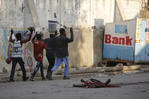 EDS NOTE: GRAPHIC CONTENT - Residents walk past a the body of a man during clashes between police and gang members at the Portail neighborhood in Port-au-Prince in Port-au-Prince, Haiti, Thursday, Feb. 29, 2024. Gunmen shot at the international airport and other targets in a wave of violence that forced businesses, government agencies and schools to close early. (AP Photo/Odelyn Joseph)