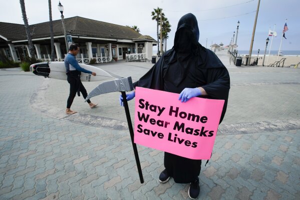 Spencer Kelly, dressed as the grim reaper, demonstrates in favor of the stay-at-home order during the coronavirus pandemic at the pier Friday, May 8, 2020, in Huntington Beach, Calif. (AP Photo/Chris Carlson)