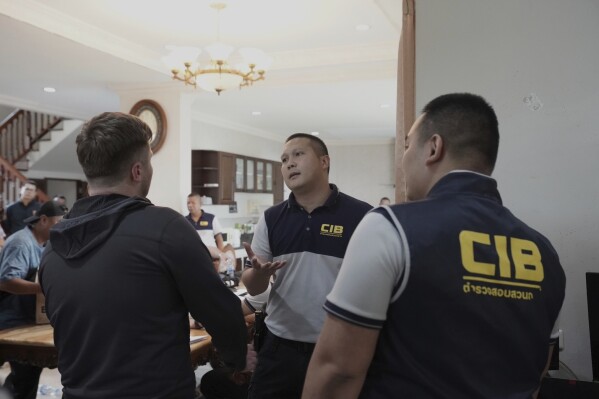 Thai Police Central Investigation Bureau personnel talk to one of the suspects, left, back to camera, at a rental house where an online investment fraud targeting Australians was allegedly being run in Samut Prakarn, Thailand, Monday, June 16, 2025. (Thailand Central Investigation Bureau via AP)