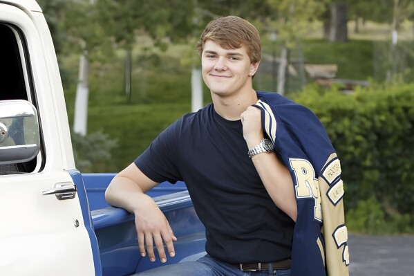 Carter Davis leans against a blue and white pickup truck and smiles for a photo with a sports jacket slung over one shoulder.