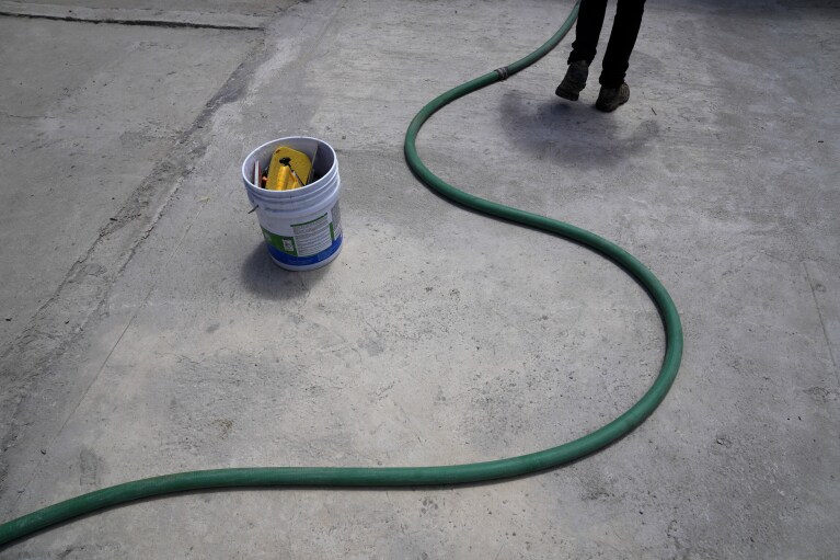 Augustin Rodriguez walks with a hose as he delivers water to a home Tuesday, May 9, 2023, in Tijuana, Mexico. Among the last cities downstream to receive water from the shrinking Colorado River, Tijuana is staring down a water crisis. (AP Photo/Gregory Bull)