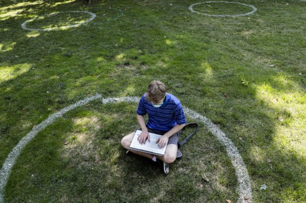 FILE - In this Aug. 25, 2020, file photo, Logan Armstrong, a junior, works while sitting inside a painted circle on the lawn of the Oval during the first day of fall classes at Ohio State University in Columbus, Ohio.   Colleges across the country are struggling to salvage the fall semester as campus coronavirus cases skyrocket and tensions with local health leaders flare. Schools have locked down dorms, imposed mask mandates, barred student fans from football games and toggled between online and in-person classes.   (Joshua A. Bickel/The Columbus Dispatch via AP, File)