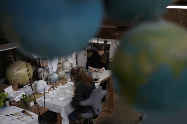 Artists make globes at a studio in London, Tuesday, Feb. 27, 2024. Globes in the age of Google Earth capture the imagination and serve as snapshots of how the owners see the world and their place in it. Peter Bellerby made his first globe for his father, after he could not find one accurate or attractive enough. In 2008, he founded Bellerby & Co. Globemakers in London. His team of dozens of artists and cartographers has made thousands of bespoke globes up to 50 inches in diameter. The most ornate can cost six figures. (AP Photo/Kin Cheung)