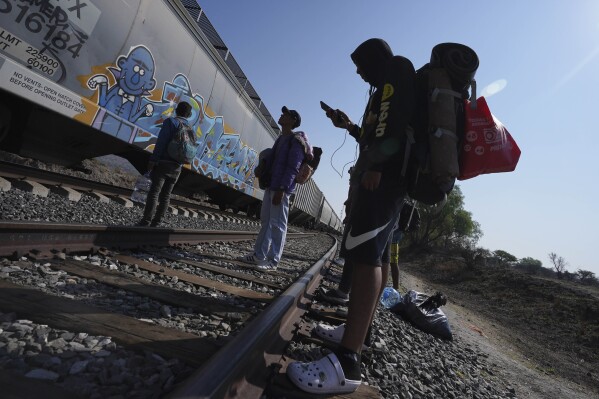 FILE - Migrants watch a train go past as they wait along the train tracks hoping to board a freight train heading north, one that stops long enough so they can hop on, in Huehuetoca, Mexico, May 12, 2023, the day after U.S. pandemic-related asylum restrictions called Title 42 were lifted. Unwittingly, migrants in Latin America finance disinformation during their journeys to the U.S., as they fall victim to fraud that can cost them thousands of dollars and that in turn has served to develop new business models, from fake work recruiters to those who call themselves "migration coaches." (AP Photo/Marco Ugarte, File)