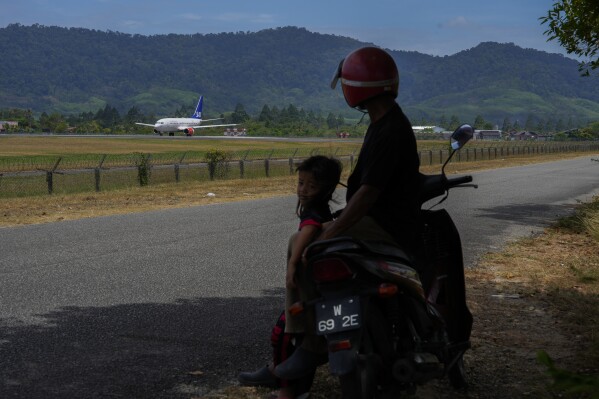 Local residents watch a Scandinavian Airlines medevac plane prepare to take off on runway at Langkawi international airport on the Malaysian resort island of Langkawi, Malaysia, Sunday, March 3, 2024. An airplane believed to be carrying Norway’s King Harald departed Malaysia on Sunday, a day after he was implanted with a pacemaker. (AP Photo/Vincent Thian)