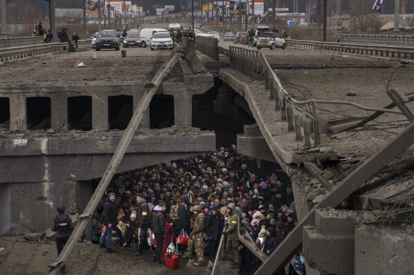 Ukrainians crowd under a destroyed bridge as they try to flee by crossing the Irpin River on the outskirts of Kyiv, Ukraine, Saturday, March 5, 2022. (AP Photo/ Emilio Morenatti)