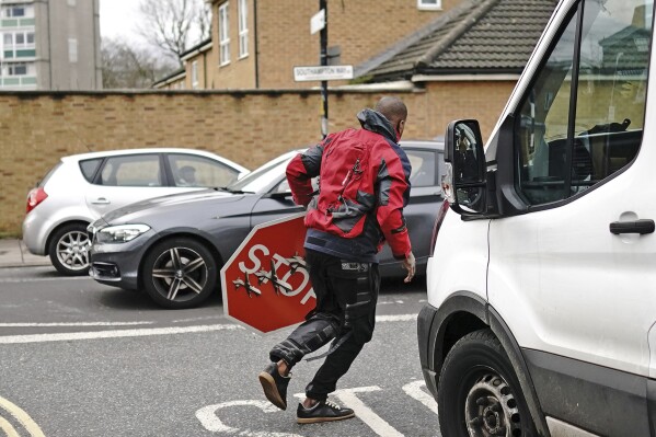 A person removes a piece of art work by Banksy, which shows what looks like three drones on a traffic stop sign, which was unveiled at the intersection of Southampton Way and Commercial Way in Peckham, south east London, Friday Dec. 22, 2023. (Aaron Chown/PA via AP)