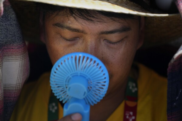 FILE - A World Youth Day volunteer uses a small fan to cool off from the intense heat, as he waits ahead of the Pope Francis arrival at Passeio Marítimo in Algés, just outside Lisbon, Sunday, Aug. 6, 2023. The last 12 months were the hottest Earth has ever recorded, according to a new report Thursday, Nov. 9, by Climate Central, a nonprofit science research group. (AP Photo/Armando Franca)