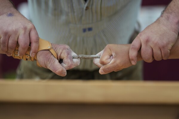 Men dressed in traditional clothes try to pull the opponent over the table at the German Championships in Fingerhakeln or finger wrestling, in Pang, near Rosenheim, Germany, Sunday, April 27, 2025. (AP Photo/Matthias Schrader)