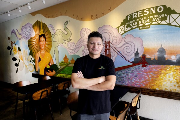 David Rasavong stands by a mural depicting his family's journey from Laos to San Francisco and then to Fresno, in his restaurant 