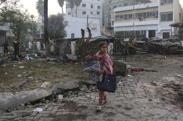 A girl carries blankets as she walks past the site of a deadly explosion at al-Ahli hospital in Gaza City, Wednesday, Oct. 18, 2023. (AP Photo/Abed Khaled)
