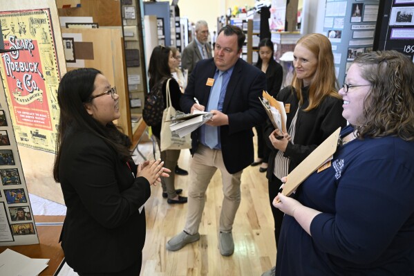 Student Alexandra Bui, left, of Temple, Texas, explains her project entitled "Turning The Page: The Sears Catalog's Impact On African Americans" to judges Sean Brennan, center, Kris Ice, second from right, and Traci Manning on Tuesday, June 11, 2024 in College Park, Md.. Bui's was one of the many exhibits on display for the National History Day event at the University of Maryland. (AP Photo/John McDonnell)