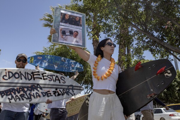 A demonstrator holds photos of the foreign surfers who disappeared during a protest in Ensenada, Mexico, Sunday, May 5, 2024. Mexican authorities said Friday that three bodies were recovered in an area of Baja California near where two Australians and an American went missing last weekend during an apparent camping and surfing trip. (AP Photo/Karen Castaneda)