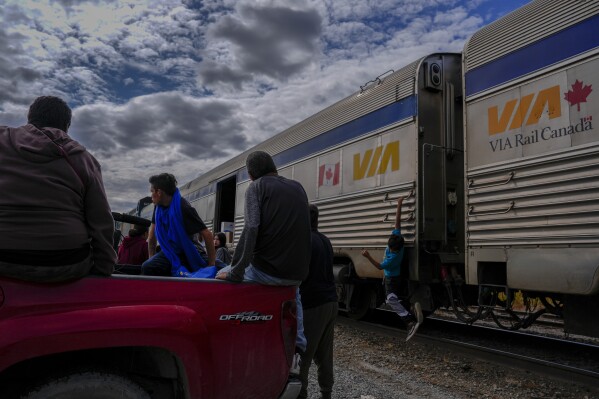 A young passenger hangs on the side of a train as others unload their belongings Friday, Aug. 9, 2024, in Thicket Portage, Manitoba. (AP Photo/Joshua A. Bickel)