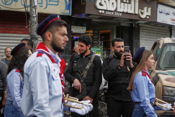 A security officer uses his cell phone to film as members of the Greek Orthodox Church in Syria march to mark Palm Sunday in the predominantly Christian al-Qassaa neighborhood of Damascus, Syria, Sunday, April 13, 2025. (AP Photo/Omar Sanadiki)