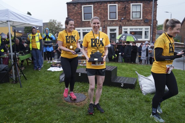 Verity Rees from Windermere, Florida, center, holds her trophy after winning the women's open category at the World Coal Carrying Championships in Ossett, West Yorkshire, England, Monday, April 21, 2025. (AP Photo/Jon Super)