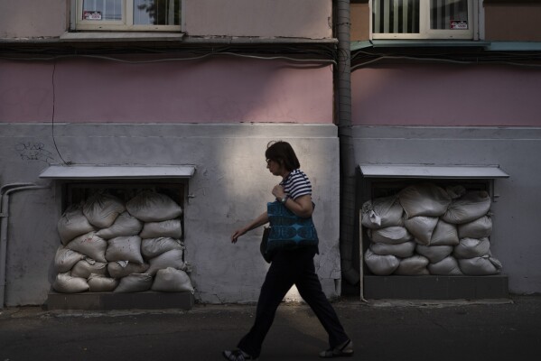 FILE - A pedestrian walks on a sidewalk past an apartment building with sandbags stacked against windows in Kyiv, Ukraine, Thursday, July 6, 2023. (AP Photo/Jae C. Hong, File)