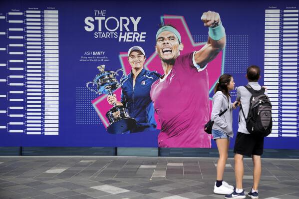 Spectators stand by an illustration of 2022 champions Ash Barty and Rafael Nadal, ahead of first round matches at the Australian Open tennis championship in Melbourne, Australia, Monday, Jan. 16, 2023. (AP Photo/Aaron Favila)