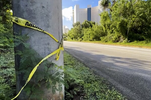 In this image taken from video, police tape is wrapped around a pole with Tsubaki Towers in the background in Tamuning, Guam, Friday, Jan. 5, 2024, after a fatal shooting on Thursday. Authorities in the U.S. territory of Guam on Friday vowed to bring to justice those who fatally shot a Korean visitor in the tourist district. (KUAM-TV via AP)