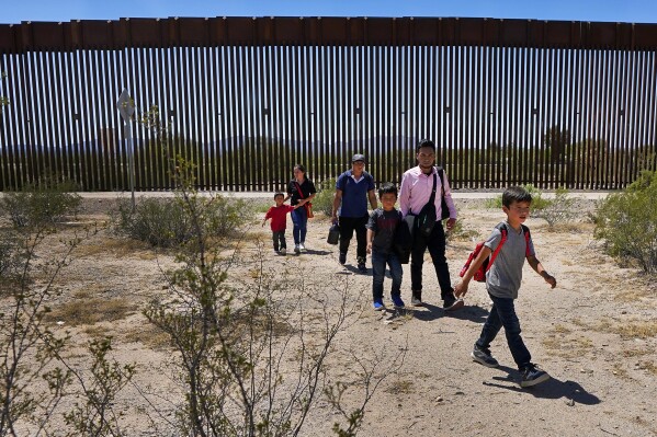 ARCHIVO - Una familia de cinco miembros que dicen ser de Guatemala y Perú, vestidos con camisas rosas, caminan por el desierto pasando el muro fronterizo en el sector de Tucson de la frontera entre Estados Unidos y México el 29 de agosto de 2023.  En el Monumento Nacional Organ Pipe Cactus, la Oficina de Aduanas y Protección Fronteriza dijo el lunes 27 de noviembre, cerca de Lukeville, Arizona, que cerrará uno de los dos puentes para vehículos en Eagle Pass, Texas, una ciudad de unas 30.000 personas.  El año fue un corredor muy transitado por los cruces ilegales.  También reduce la entrada de vehículos al remoto cruce del desierto en Lukeville, que se ha convertido en una importante ruta migratoria en los últimos meses.  (Foto AP/Matt York, archivo)