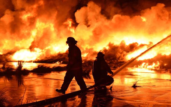 Firefighters work on a fire burning at the former Market Street Wharf early Sunday, Oct. 17, 2021, in New Orleans. The remains of an abandoned river wharf went up in flames over the weekend in New Orleans as fireworks went off nearby, but officials haven’t yet determined whether the display played a role in the enormous fire. (Chief C. Mickal/New Orleans Fire Department Photo Unit via AP)