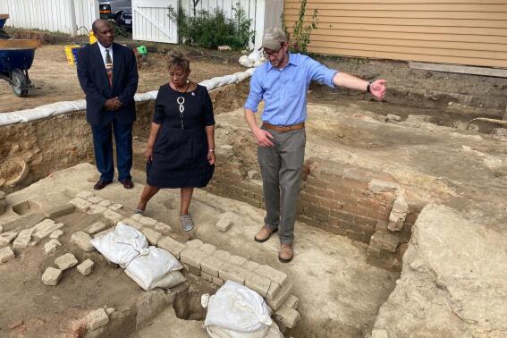 FILE - From left, Reginald F. Davis, pastor of First Baptist Church, Connie Matthews Harshaw, a member of First Baptist, and Jack Gary, Colonial Williamsburg's director of archaeology, stand at the brick-and-mortar foundation of one the oldest Black churches in the U.S. on Oct. 6, 2021, in Williamsburg, Va. Experts announced Thursday, April 6, 2023, that three men whose graves were found at the site were members of the church in the early 19th Century. (AP Photo/Ben Finley, File)