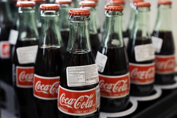 FILE - In this July 9, 2015, file photo, bottles of Coca-Cola are on display at a Haverhill, Mass., supermarket. Coca-Cola has announced plans to shutter a bottling plant in Northampton, Mass., in the summer of 2023, leaving its 319 employees to find new jobs. (AP Photo/Elise Amendola, File)