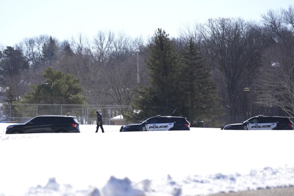 A police officer walks across a road after two police officers and a first responder were shot and killed Sunday, Feb. 18, 2024, in Burnsville, Minn. (AP Photo/Abbie Parr)