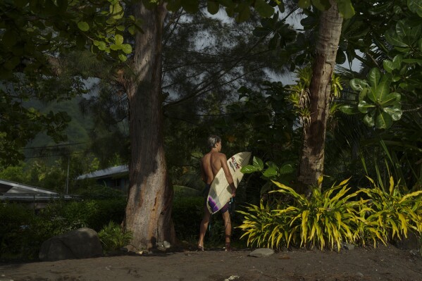 A surfer walks along the beach in Teahupo'o, Tahiti, French Polynesia, Monday, Jan. 15, 2024. (AP Photo/Daniel Cole)