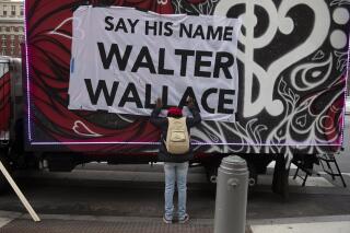FILE - In this Nov. 4, 2020, file photo, Sheila Rhames rests her hands on a banner honoring Walter Wallace Jr. in Philadelphia Wallace, a Black man, was shot and killed by police in West Philadelphia in October of 2020. Rhames was his neighbor. The Philadelphia Inquirer reported Tuesday, Oct. 26. 2021, the anniversary of the fatal police shooting of Wallace, that Philadelphia will spend $14 million to equip all of its officers with stun guns, train them on how to use them and require officers to wear them while on duty. (Joe Lamberti/Camden Courier-Post via AP, File)