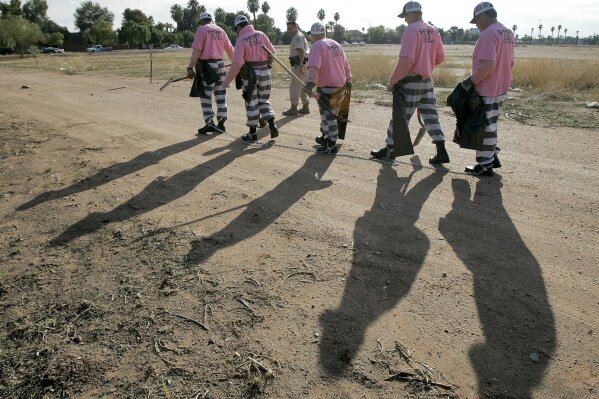 FILE- In this Dec. 11, 2007, file photo, members of the Maricopa County DUI chain gang are escorted to their assignment in Phoenix. National lawmakers are expected on Wednesday, Dec. 2, 2020, to introduce a joint resolution aimed at striking language from the U.S. Constitution that enshrines a form of slavery in America’s foundational documents. Many Americans will recognize modern-day prison labor as chain gangs deployed from prison facilities for agricultural and infrastructure work. (AP Photo/Matt York, File)