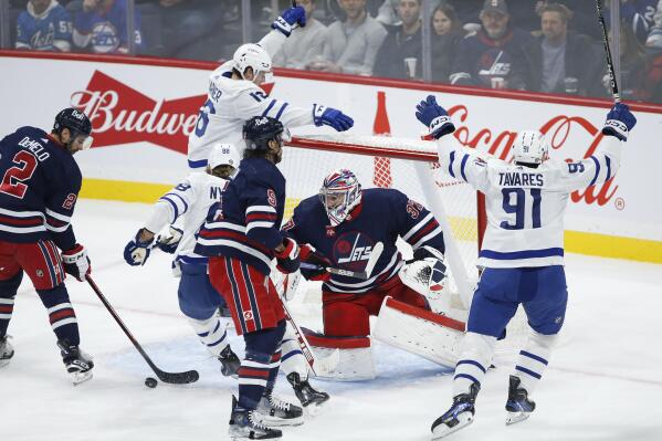 Toronto Maple Leafs' John Tavares (91) and Mitchell Marner (16) celebrate Tavares' goal against Winnipeg Jets goaltender Connor Hellebuyck (37) during the first period of an NHL hockey game Saturday, Oct. 22, 2022, in Winnipeg, Manitoba. (John Woods/The Canadian Press via AP)