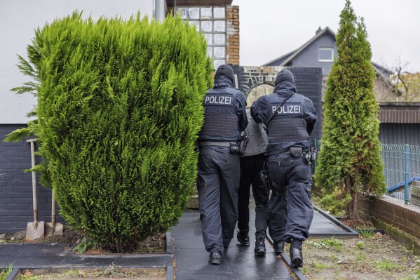 CORRECTS CAPTION INFORMATION - Police officers take a suspect back to a house during a raid in Garbsen, Germany, Thursday, Nov. 23, 2023. German police arrested two men Thursday in connection with organized smuggling of migrants during raids in Berlin and the northern state of Lower Saxony. About 260 officers were involved in the raids in which 14 properties were searched, eight in Lower Saxony and six in Berlin. (Ole Spata/dpa via AP)